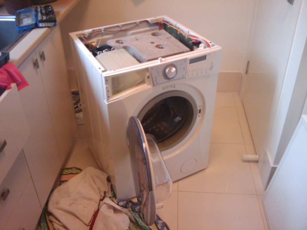 A broken washing machine is shown with not top cover.