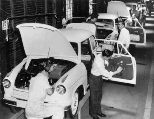 A black and white photo of male assembly-line workers constructing cars is shown here.