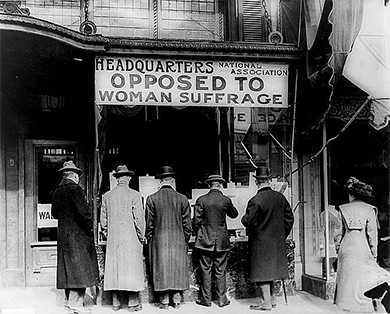 A photograph shows five men and a woman standing outside of a building labeled 
