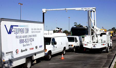 The picture shows a series of trucks headed in one direction. A truck pointed in the opposite direction has a crane with a device over the middle truck.